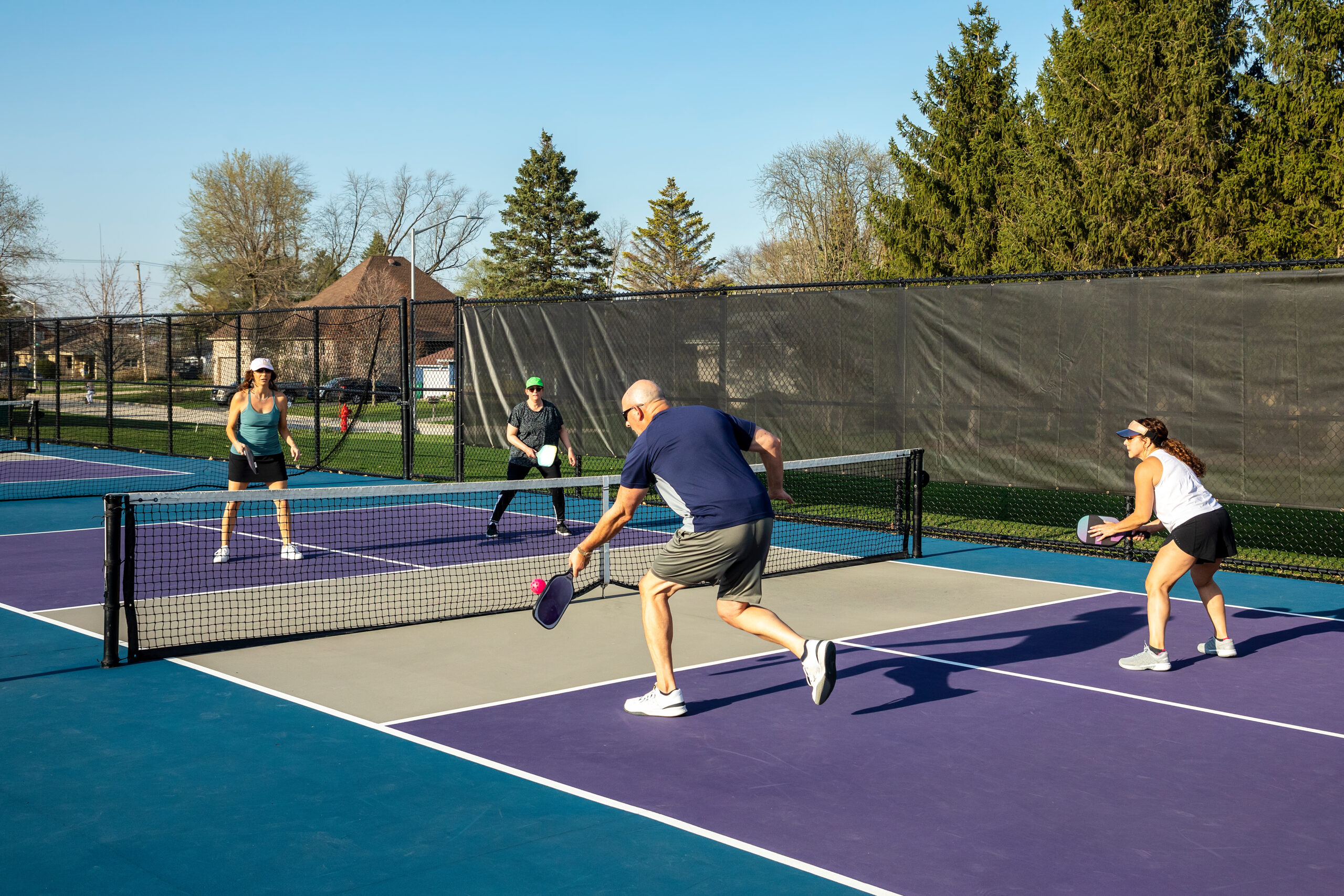 A male player returns a volley at the net on a dedicated pickleball court at a public park.