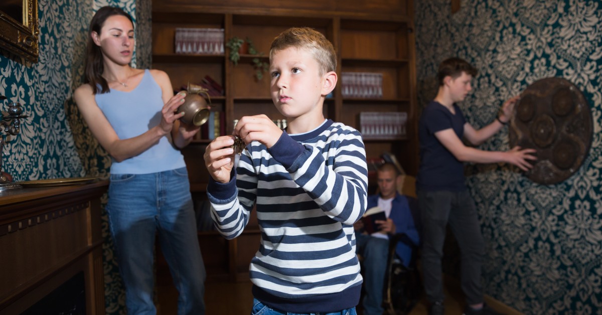 Two adults and two kids inspect different objects in a small room. A woman behind a young boy examines the inside of an urn.